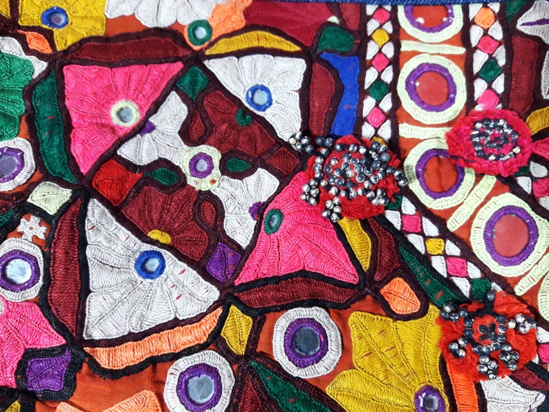 May include: A colorful textile with intricate embroidery and mirror embellishments. The fabric features a variety of geometric and floral patterns in shades of red, pink, green, blue, yellow, and white.