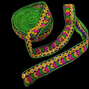May include: Green, yellow, pink, and blue embroidered trim with mirrored accents. The trim is rolled up and ready to be used for sewing or crafting.