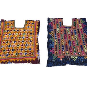 Puede incluir: Dos tops bordados coloridos con escotes cuadrados. Uno es amarillo con un patrón geométrico y el otro es azul oscuro con detalles de espejo. Ambos tienen flecos decorativos y costuras intrincadas.