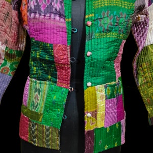 Puede incluir: Una chaqueta acolchada de patchwork con cierre de bot&oacute;n. La chaqueta est&aacute; hecha de varias telas en tonos de verde, morado, rosa y marr&oacute;n. La tela tiene un patr&oacute;n tejido.