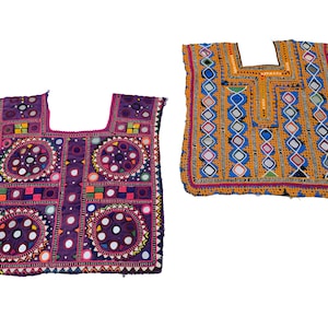 Può includere: Due top tessili ricamati colorati. Uno è viola con accenti di specchi circolari e motivi geometrici. L'altro è giallo con motivi a rombi blu, bianchi e rossi e accenti di specchi. Entrambi hanno scollature quadrate.