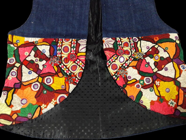 May include: A denim vest with colorful embroidered floral patterns and mirrored accents. The vest has a black lining with a dotted pattern.