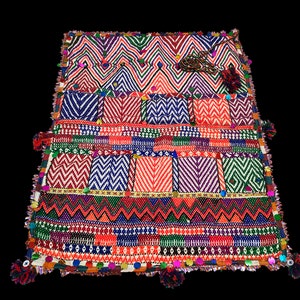 May include: A colorful woven tapestry with geometric patterns in shades of red, blue, green, and white. The tapestry has a fringe border with tassels and beads.
