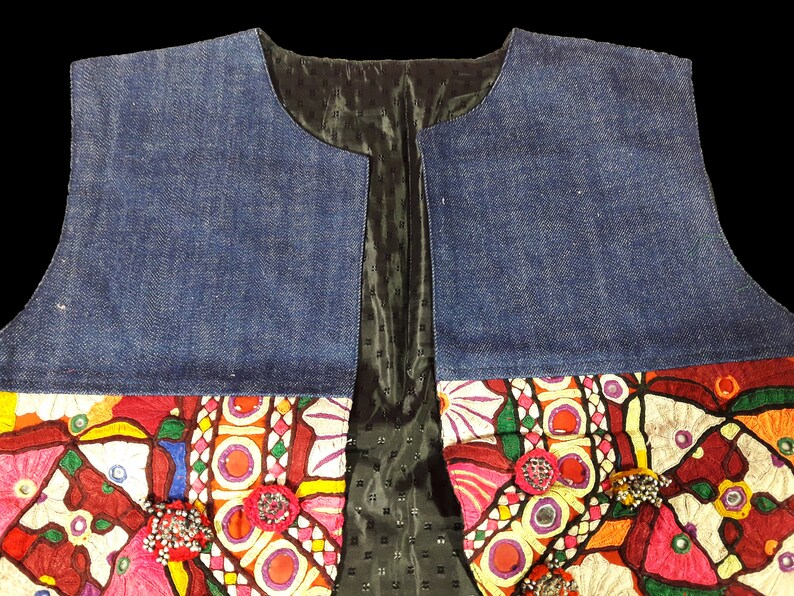 May include: A denim vest with colorful embroidery and embellishments. The vest has a black lining and a V-neck.