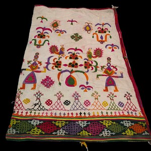 Puede incluir: Una tela de algodón blanca con bordados coloridos que representan figuras estilizadas, pájaros y motivos florales. El bordado se realiza en una variedad de colores, incluyendo rojo, verde, azul, amarillo y rosa. La tela tiene un borde con flecos.