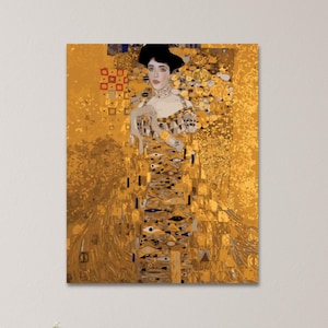 May include: A framed print of a Gustav Klimt painting, featuring a woman in a gold dress and black hat. The artwork has a gold background with geometric and organic patterns. The woman is adorned with jewelry and has a serious expression.