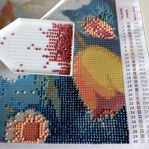 a diamond-pointing tool filled with red and orange beads, placed on a colorful mosaic canvas. The canvas is a vibrant display of various patterns and designs, creating a visually striking and intricate work of art.