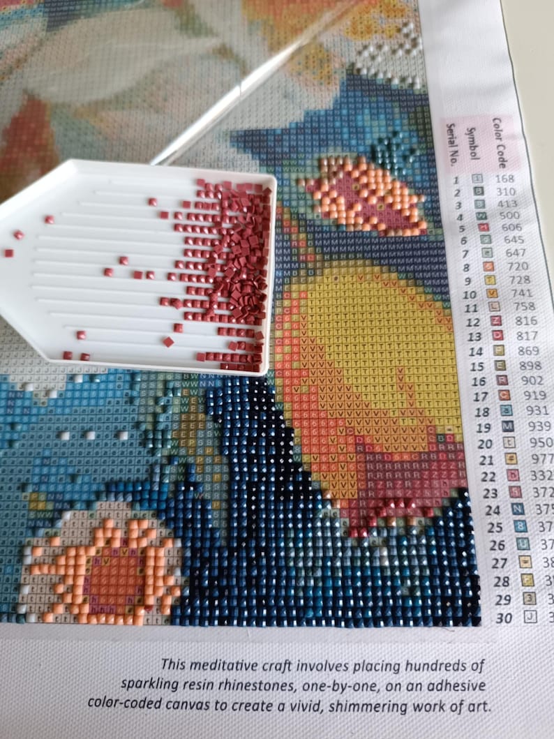 a diamond-pointing tool filled with red and orange beads, placed on a colorful mosaic canvas. The canvas is a vibrant display of various patterns and designs, creating a visually striking and intricate work of art.