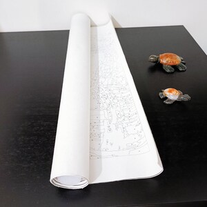 a roll of paper with a drawing of a turtle on it, placed on a black surface next to two small turtle figurines.