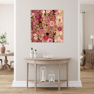 May include: Abstract art print with a pattern of overlapping circles in pink, gold, and black. The artwork hangs on a white wall above a wooden console table, creating a modern interior design. The artwork is a square.