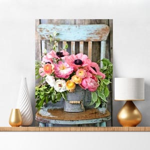 May include: A bouquet of pink, orange, and white flowers in a galvanized metal bucket with a wooden handle, placed on a distressed light blue wooden chair. The arrangement features lush green foliage and is displayed as a decorative print.