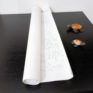a roll of paper with a drawing of a turtle on it, placed on a black surface next to two small turtle figurines.