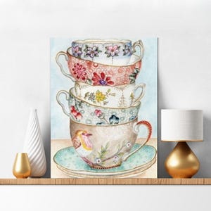May include: A vertical wall art print featuring a stack of four decorative teacups on a saucer. The top cup is white with purple flowers, the second is coral with floral patterns, the third is white with yellow flowers, and the base cup features a robin bird.