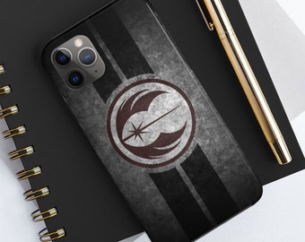 Puede incluir: Una funda de teléfono negra con un fondo gris y negro desgastado. La funda presenta un símbolo blanco y rojo con una estrella y dos alas. El símbolo está rodeado por un círculo negro.