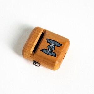 May include: A wooden case with a sliding lid and a small metal loop. The case has a black and white graphic of a TIE fighter from Star Wars.
