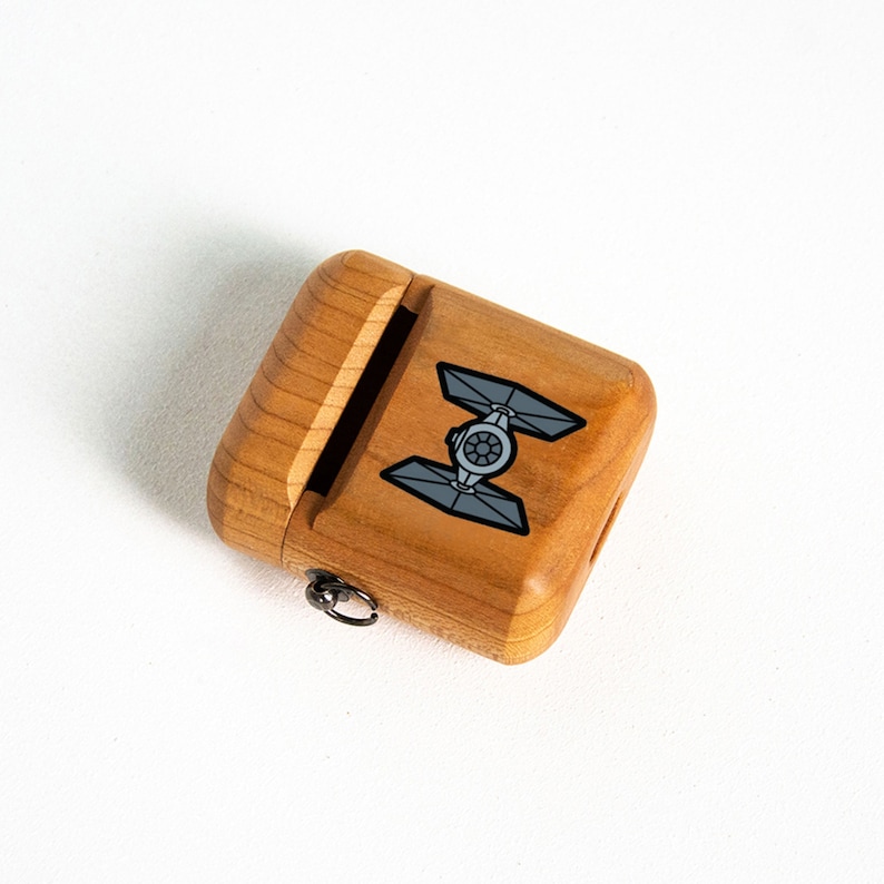 May include: A wooden case with a sliding lid and a small metal loop. The case has a black and white graphic of a TIE fighter from Star Wars.