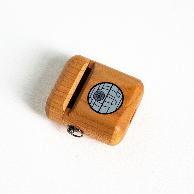May include: A wooden case with a sliding lid and a metal ring for attaching a keychain. The case has a black and white image of the Death Star from Star Wars.