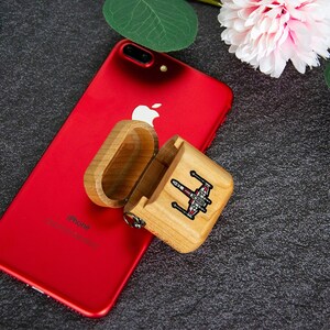 May include: A wooden case with a Star Wars X-Wing fighter design on the lid. The case is open and is sitting on top of a red iPhone.