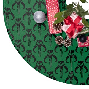 May include: Green Christmas tree skirt with a repeating black graphic pattern. The skirt is decorated with wrapped gifts, pinecones, and a silver ornament. The gifts are wrapped in red paper with white stars and a red bow.
