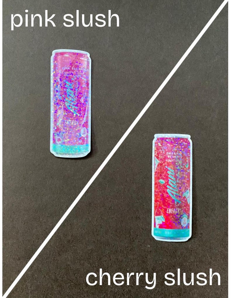 May include: Two colorful aluminum cans with a glittery finish. The can on the left is pink and says "Pink Slush" and the can on the right is red and says "Cherry Slush".