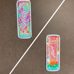 May include: Two colorful can stickers with glitter. The first sticker is pink and green with the text "Cherry Twist" and the second sticker is orange and red with the text "Strawberry Sunrise".