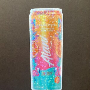 May include: A sticker of a can of Aloha Energy drink. The can is blue, pink, and orange with a glittery finish. The can has a tropical design with a pineapple, orange slices, and palm trees. The text on the can reads "Aloha Energy" and "Orange Kiss".