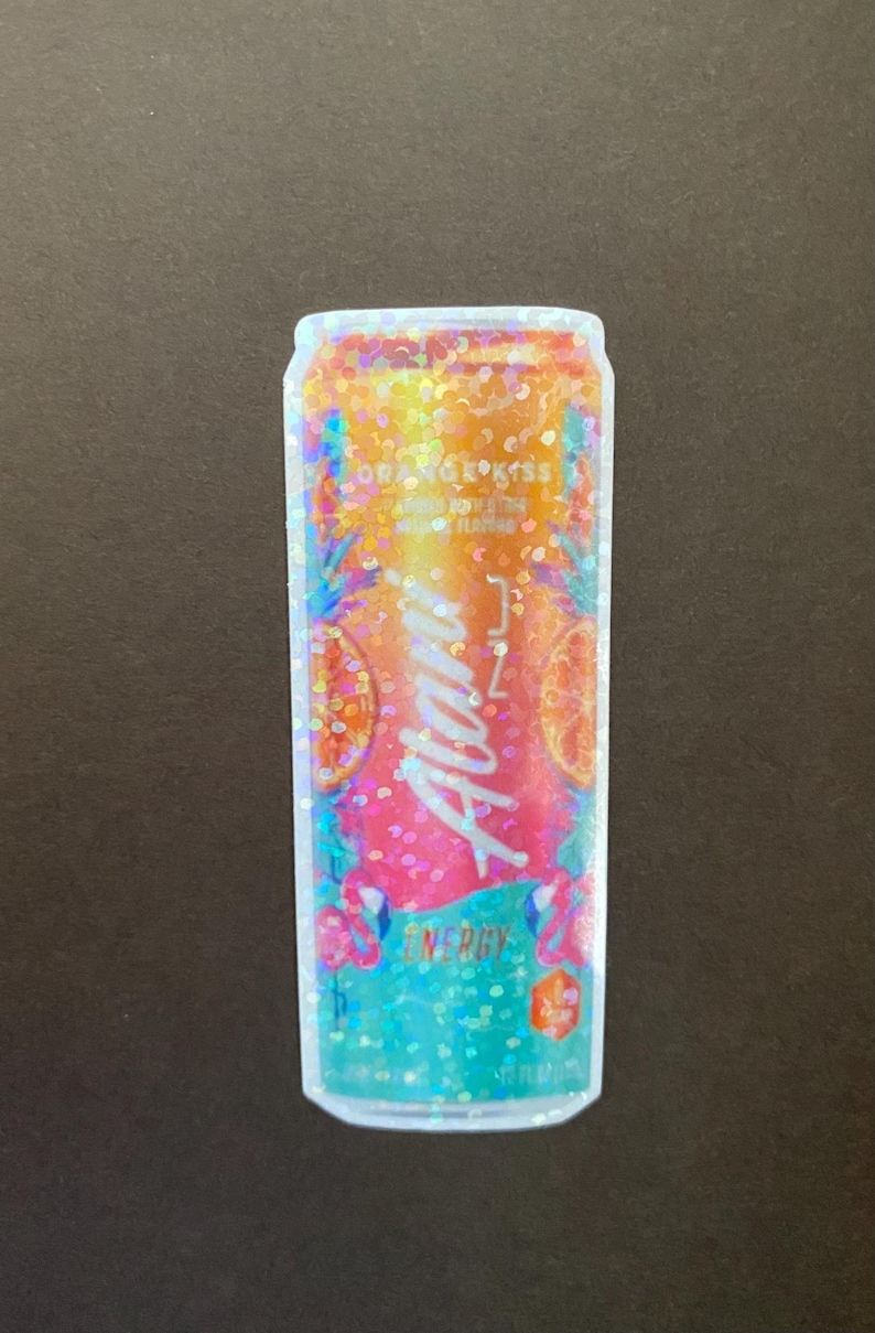 May include: A sticker of a can of Aloha Energy drink. The can is blue, pink, and orange with a glittery finish. The can has a tropical design with a pineapple, orange slices, and palm trees. The text on the can reads "Aloha Energy" and "Orange Kiss".