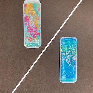 May include: Two aluminum cans with glitter designs. The can on the left is orange and pink with the text "Aloha" and "Sherbet Swirl". The can on the right is blue with the text "Aloha" and "Blue Slush".