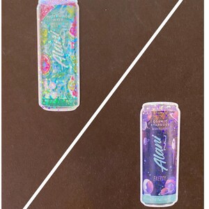 May include: Two colorful, glittery, aluminum cans with a holographic effect. The can on the left says "Watermelon Wave" and the can on the right says "Cosmic Stardust". Both cans are decorated with a design that matches the flavor.