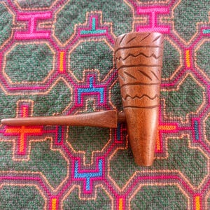 Puede incluir: Una pipa de fumar de madera marrón con un hornillo cilíndrico que presenta líneas onduladas horizontales talladas y una boquilla lisa y cónica. La pipa está fabricada en una sola pieza de madera pulida, mostrando una veta natural y un tono marrón.