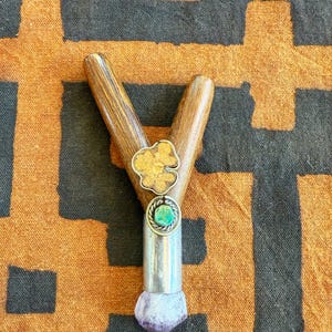 May include: A wooden Y-shaped pipe with decorative silver and gemstone accents. The pipe features a silver band with a turquoise stone, a gold-colored flower-shaped accent, and a purple amethyst crystal at the base.