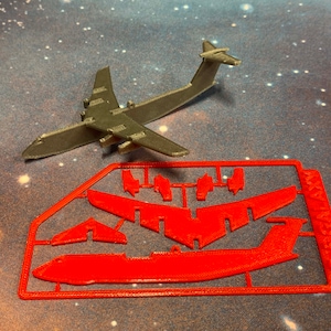 May include: A gray plastic model airplane and a red plastic model kit. The assembled airplane is on top, with the unassembled kit below. The kit includes the airplane's wings, tail, and fuselage. The text "ICE GALAXY" is visible on the kit.