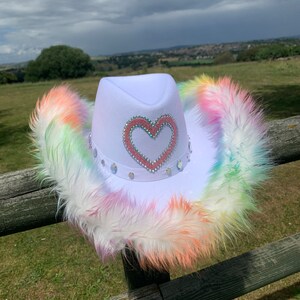 May include: White cowboy hat with a pink heart design and rainbow colored fur trim.