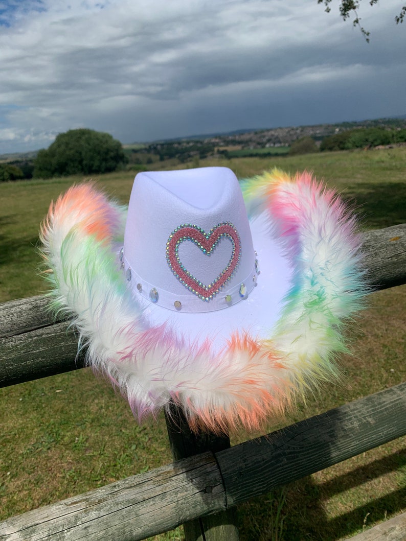 May include: White cowboy hat with a pink heart design and rainbow colored fur trim.