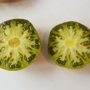 May include: Two halves of a green tomato, cut in half, showing the inside of the tomato with seeds and a yellow centre.