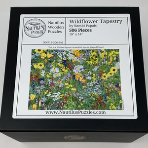 May include: A black box featuring a colorful Wildflower Tapestry jigsaw puzzle by Bambi Papais. The puzzle contains 506 pieces and measures 19 inches by 14 inches. The box also displays the Nautilus Wooden Puzzles logo and website.