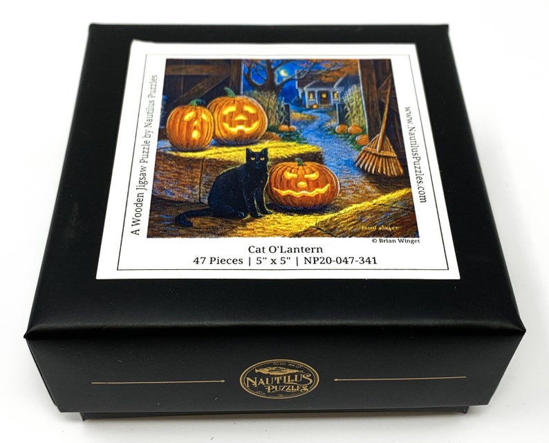 May include: A black cat sits near a jack-o-lantern in a barn setting. The 47-piece wooden jigsaw puzzle is titled "Cat O'Lantern" and measures 5 inches by 5 inches.