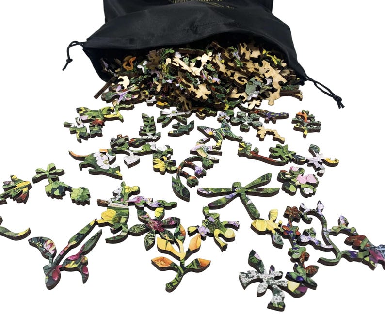 May include: Wooden jigsaw puzzle pieces with floral and leaf designs spill from a black drawstring bag. The pieces feature vibrant colors and intricate details, including flowers, leaves, and a dragonfly. The puzzle appears to be nature-themed.