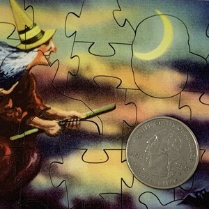 Może przedstawiać: Element układanki z ilustracją w stylu vintage przedstawiającą wiedźmę na miotle na tle nocnego nieba z p&oacute;łksiężycem. Z przodu znajduje się moneta o nominale 25 cent&oacute;w.