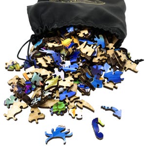 May include: A black drawstring bag spilling out wooden jigsaw puzzle pieces. The pieces are various shapes and sizes, with vibrant blue, green, and yellow painted designs. Some pieces are scattered around the bag.