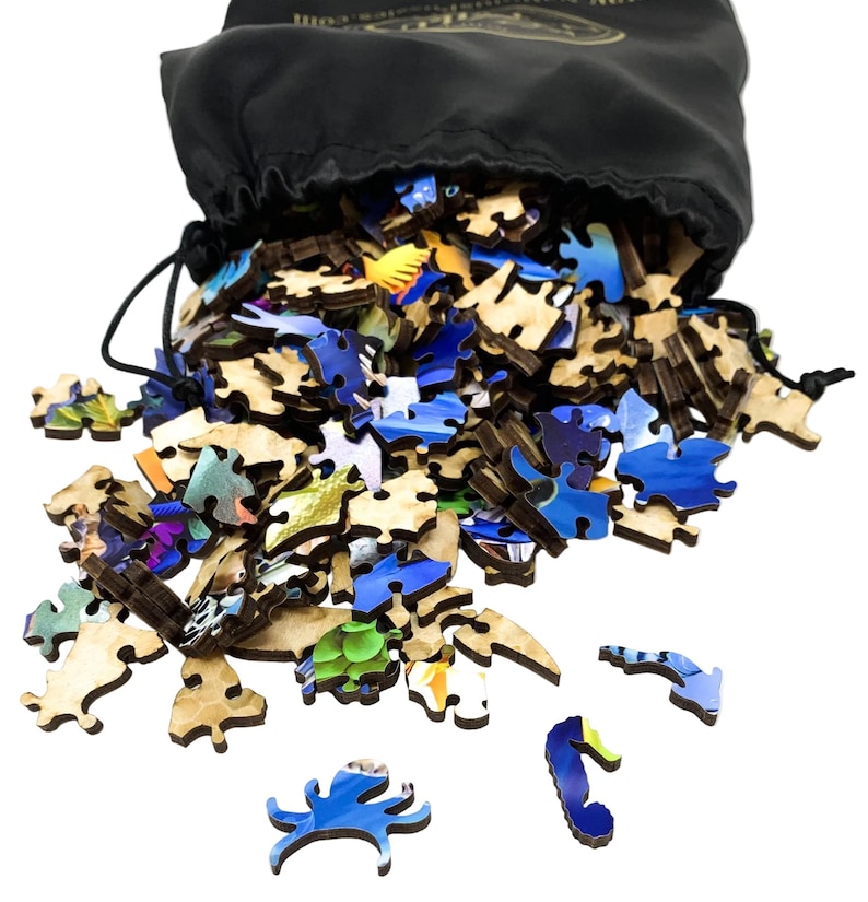 May include: A black drawstring bag spilling out wooden jigsaw puzzle pieces. The pieces are various shapes and sizes, with vibrant blue, green, and yellow painted designs. Some pieces are scattered around the bag.