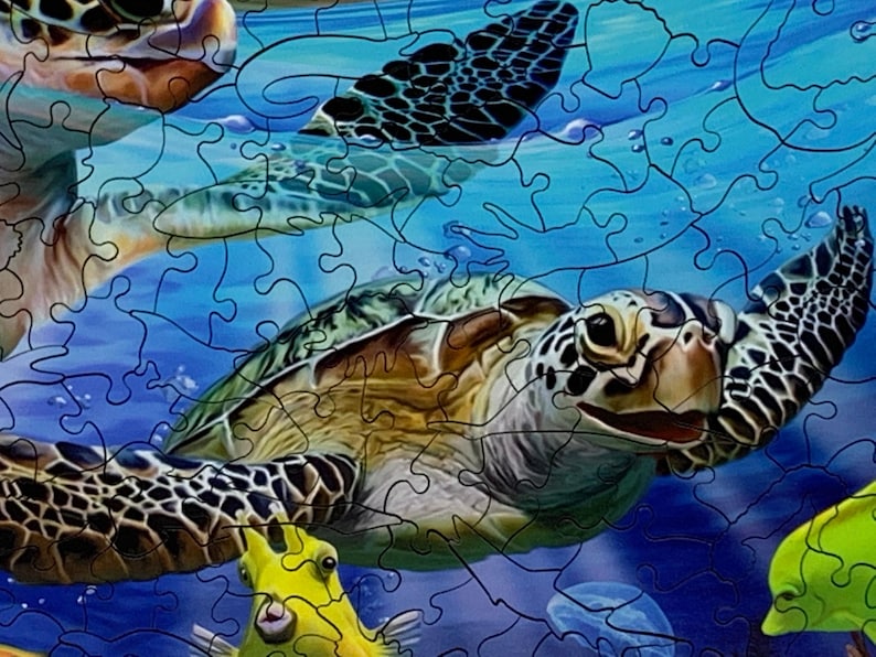 May include: A completed jigsaw puzzle featuring sea turtles swimming underwater. The puzzle pieces are interlocked, depicting turtles with patterned shells, surrounded by blue water and yellow fish. The image is a close-up view.
