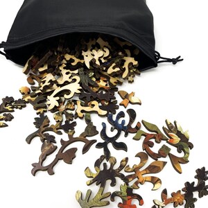 May include: A black drawstring bag with a gold logo that says "Nautical Puzzle Co. Est. 2018" is spilling out wooden jigsaw puzzle pieces with a floral design.