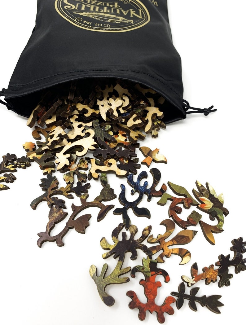 May include: A black drawstring bag with a gold logo that says "Nautical Puzzle Co. Est. 2018" is spilling out wooden jigsaw puzzle pieces with a floral design.