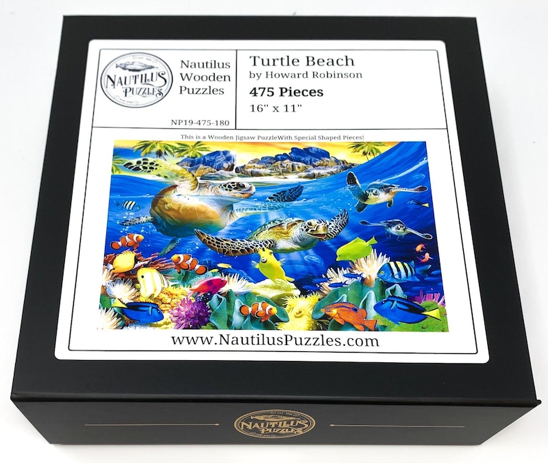 May include: A black box featuring a jigsaw puzzle titled "Turtle Beach" by Howard Robinson. The puzzle image depicts sea turtles, colorful fish, and coral in an underwater scene. The puzzle has 475 pieces and measures 16" x 11".