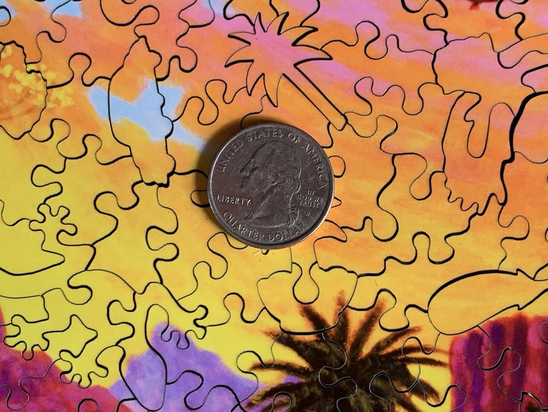 May include: A quarter coin rests on a colorful jigsaw puzzle. The puzzle features an abstract design with warm tones of yellow, orange, and purple, with black outlines. The puzzle's design includes shapes resembling palm trees and starbursts.