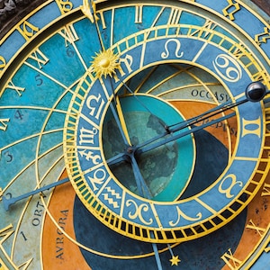 May include: Close-up of an astronomical clock face with a blue and gold design. The clock features Roman numerals, zodiac symbols, and a sunburst. The hands point to the time. The clock's face is a mix of blue, gold, and orange.