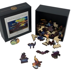 Może przedstawiać: Drewniane puzzle firmy Nautilus Puzzles, z pudełkiem przedstawiającym obrazek z puzzli i luźnymi elementami. Puzzle przedstawiają wiedźmę na miotle pod oświetlonym księżycem niebem. Zawiera 50 element&oacute;w, z elementami w kształcie dyni, kota i nietoperza.