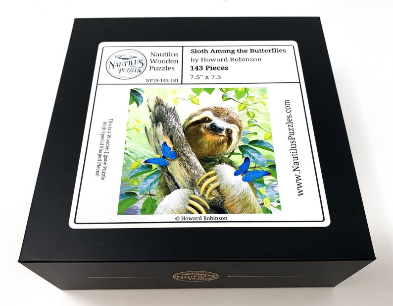 May include: A black box featuring a jigsaw puzzle with a sloth among butterflies. The puzzle, titled "Sloth Among the Butterflies" by Howard Robinson, contains 143 pieces and measures 7.5" x 7.5". The box also displays the Nautilus Puzzles logo.