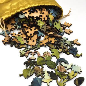 May include: A wooden jigsaw puzzle with a colorful image of a landscape scene. The puzzle pieces are scattered on a white surface and spilling out of a yellow drawstring bag.